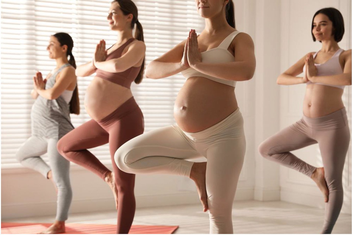 Pregnant women in prenatal yoga class practicing tree pose with hands in prayer position